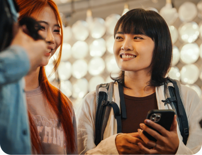 Two women walk a busy urban street while holding a cell phone