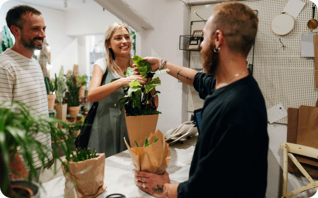 A group of customers brings several plants up to be purchased at the counter of a retail store