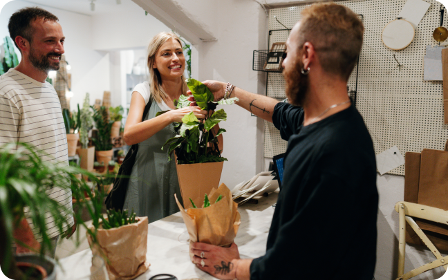 A group of customers brings several plants up to be purchased at the counter of a retail store